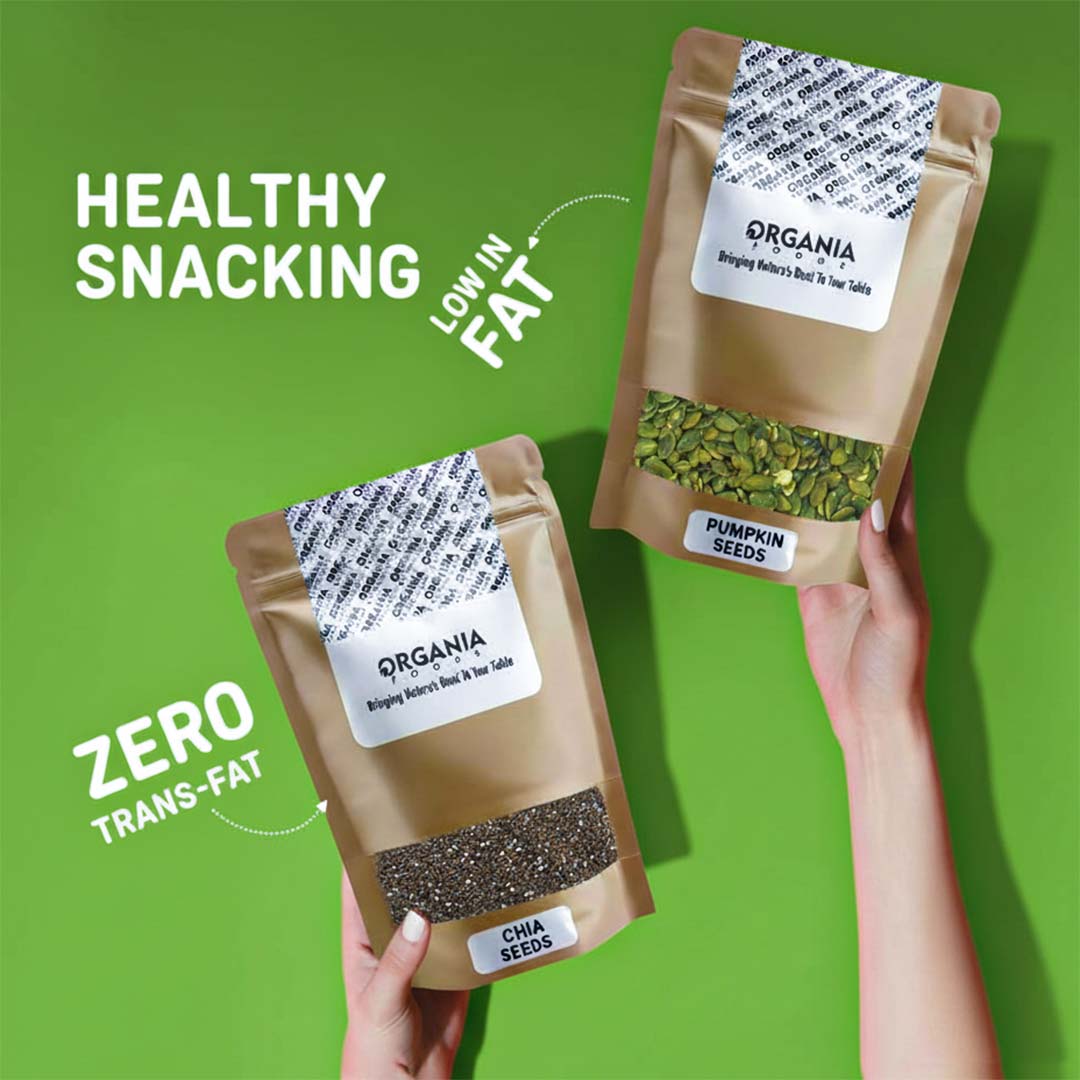 Two packages of Organia pumpkin seeds held by hands against a green background with text about healthy snacking.