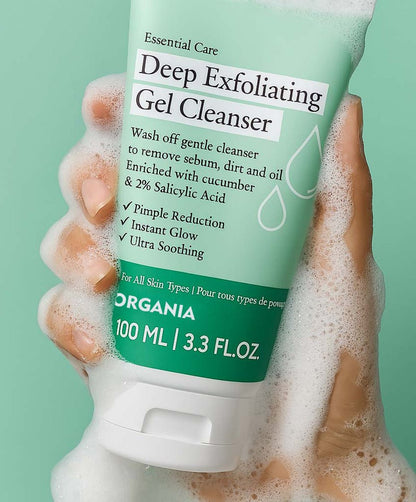 Hand holding a tube of Deep Exfoliating Gel Cleanser with a green background