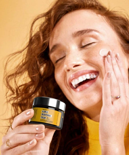 Woman applying cream to her face with a jar of cream in her hand against a warm background