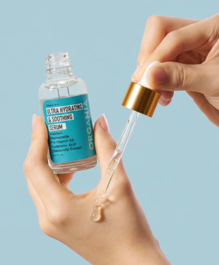 Hand holding a dropper with ultra hydrating serum against a light blue background